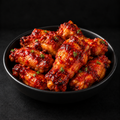 Fresh chicken wings in glossy red firecracker sauce served in a black bowl on a dark background