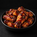 Sticky BBQ fresh chicken wings glazed in signature BBQ sauce in a black bowl on a dark background